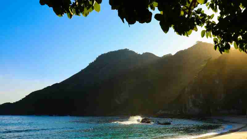 Tranquil beach scene in East Nusa Tenggara, Indonesia, featuring sunlit hills and calm waters., tags: door eilanden - pexel